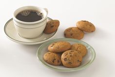 some cookies on a plate next to a cup of coffee and saucer with chocolate chips