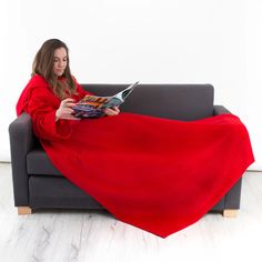 a woman sitting on a couch with a red blanket over her and reading a magazine