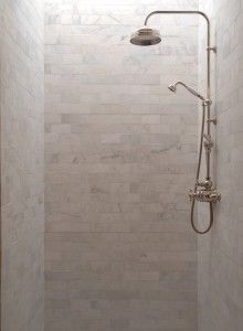 a walk in shower sitting next to a white tiled wall and floor covered in tile