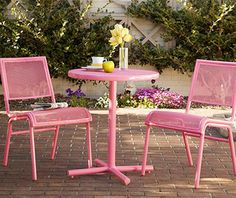 two pink chairs and a small table on a brick patio with flowers in the background