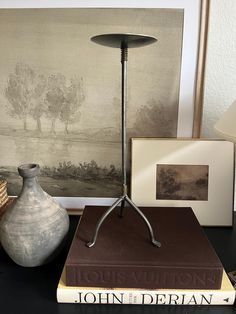 a table topped with books and a vase next to a painting on top of a wall