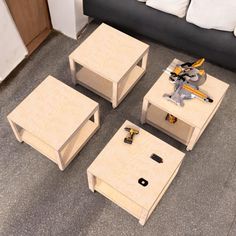 four wooden tables sitting on top of a carpeted floor next to a black couch