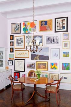 a dining room table and chairs in front of a wall with many pictures on it