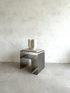 a small table with a cup on it in front of a white wall and concrete floor