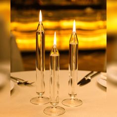 three clear candles sitting on top of a table next to silver utensils and forks