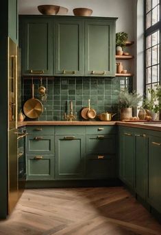 a kitchen with green cabinets and wooden floors, gold pulls on the cupboards as well as pots and pans