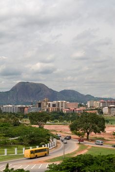 a yellow bus driving down a street next to tall buildings and green hills in the background