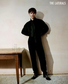 a man standing in front of a table wearing a black shirt and tie with his hands on his hips