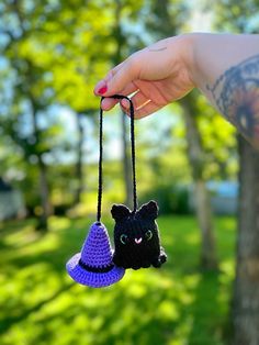 a hand holding two small crocheted items in the shape of cats and witches