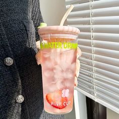 a woman holding up a drink in front of a window with blinds on the outside