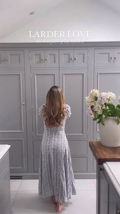 a woman is standing in the middle of a kitchen with gray cabinets and white flowers