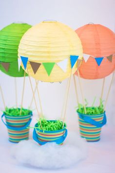 three paper hot air balloons with green grass in the middle and blue buckets below