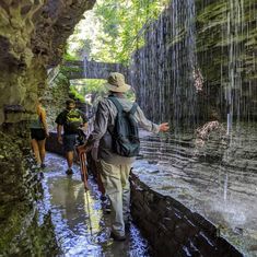 two people are walking in the water near a waterfall