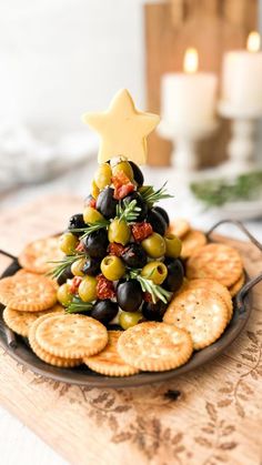 a christmas tree made out of olives and crackers on a plate with candles in the background