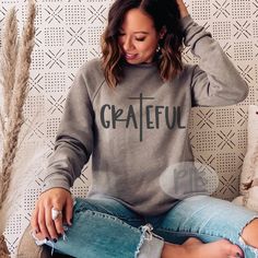 a woman sitting on top of a couch wearing a grey sweatshirt and ripped jeans with the word grateful printed on it