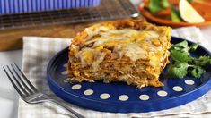 a piece of lasagna on a blue plate next to a salad and fork