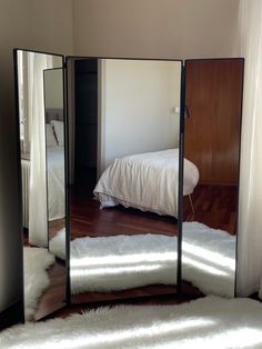 a mirror that is on the floor in front of a bed with white fluffy rugs