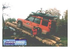 a red van parked on top of a pile of logs with a bike strapped to the roof