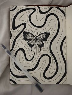 an open notebook with a black and white butterfly drawn on the cover next to a pen