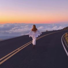 a woman is walking down the road at sunset