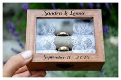 two wedding rings in a wooden box with lace on the bottom and gold bells at the top