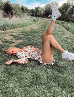 a woman laying on the grass with her legs up in the air while wearing white tennis shoes