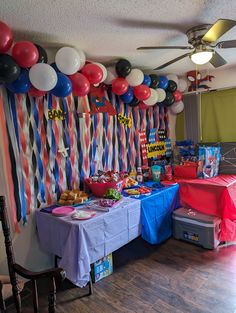 a party room with balloons and streamers on the wall, table covered in food