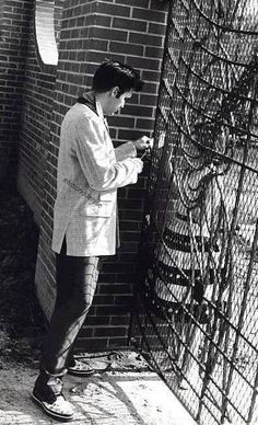 a man standing in front of a brick wall with writing on it and looking at his cell phone