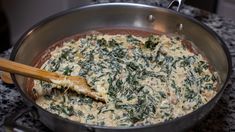 a pan filled with spinach and cheese on top of a stove next to a wooden spoon