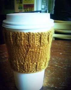 a knitted coffee cup sleeve sitting on top of a wooden table