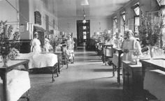 an old black and white photo of people in a room with flowers on the tables