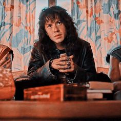 a man with long hair sitting on a couch next to a book and coffee cup