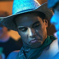 a man wearing a blue cowboy hat looking at his cell phone while standing in front of other people