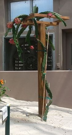 a wooden cross in front of a building with flowers growing on the outside and inside