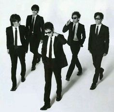 a group of young men in suits and sunglasses walking down a white floor with their hands on their hips