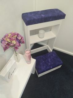 a white shelf with purple cushions next to a flower vase and candle holder on it