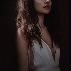 a woman with long brown hair wearing a white dress and posing for a photo in front of a dark background