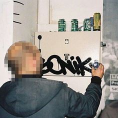 a man is writing graffiti on the wall in front of a refrigerator door with spray paint