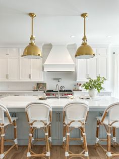 a kitchen with white cabinets and gold pendant lights hanging over the island in front of it