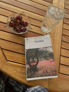 a book sitting on top of a wooden table next to a bowl of cherries