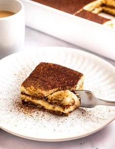 a piece of cake on a plate with a fork and cup of coffee in the background