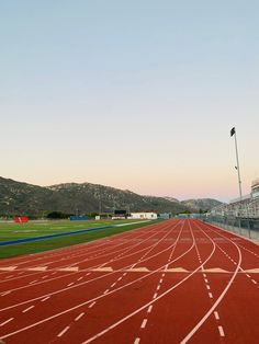 an empty track in the middle of a stadium with mountains in the background at sunset