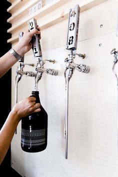 a person is holding a beer in front of two wall mounted faucets with numbers on them