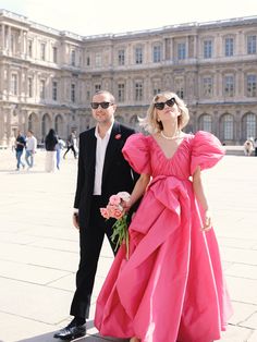 a man and woman in formal wear standing next to each other on a sidewalk near a large building