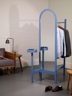 a blue coat rack stands next to a chair and table with clothes hanging on it