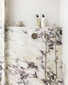 a bathroom with marbled walls and flooring, including a shower head in the middle