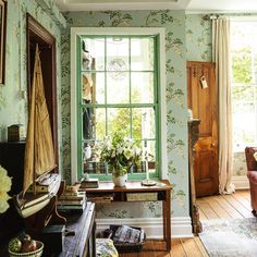 a living room filled with furniture next to a large window covered in green wallpaper