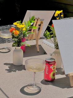 an easel and two empty wine glasses on a table with flowers in the background