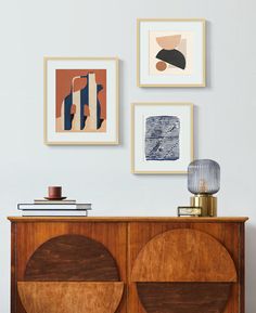 a sideboard with pictures on the wall above it and a lamp next to it