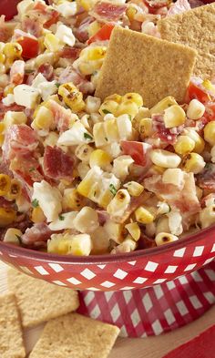 a red bowl filled with corn salad and crackers